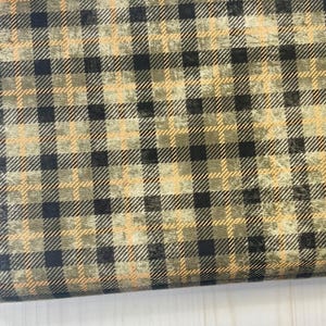 May include: Close-up of a fabric with a plaid pattern in shades of black, olive green, and tan. The fabric has a textured appearance. The text "ECLECTIC ELEMENTS" and "REGIONS BEYOND" is visible on the edge.
