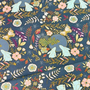 May include: Dark teal fabric with a repeating pattern of flowers, butterflies, rabbits, and foliage in shades of pink, gold, and white. The design includes full moons and a starry background. The fabric is folded, showing the pattern's repeat.