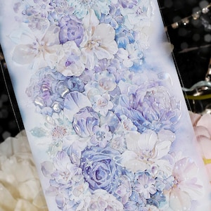 May include: A decorative sticker featuring a watercolor floral arrangement. The design showcases a variety of flowers in shades of white, lavender, and blue. The sticker has a glossy finish and a soft, dreamy aesthetic.