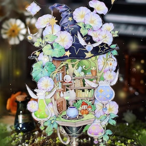 May include: A decorative acrylic standee featuring a dark blue witch hat adorned with light purple morning glory flowers and gold stars. The design includes a small interior room with bookshelves, a cauldron, and three floating potion bottles.