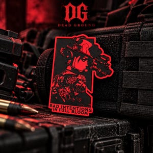 May include: A rectangular morale patch featuring a black and red graphic of a person wearing tactical gear and a headset, with a floral tattoo design on their back. The text reads BAD INTENTIONS IN FULL BLOOM in bold lettering.