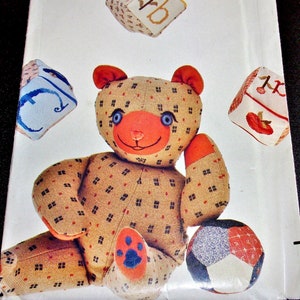 May include: A vintage craft pattern for a teddy bear and alphabet blocks. The pattern is from Butterick and is number 4685. The teddy bear is brown with a white and red face and blue eyes. The blocks are red, white, and blue with embroidered letters and designs.