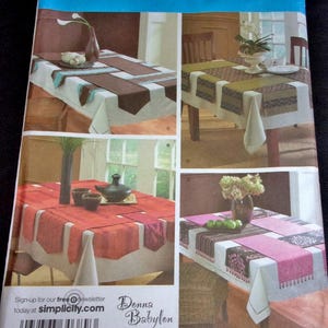 May include: Simplicity sewing pattern featuring table runner designs. The pattern includes various color and pattern options, with rectangular and square shapes. The text "Donna Babylon" is visible. The pattern is one size.