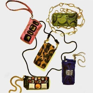 May include: Collection of cell phone cases in various designs. Includes a pink snakeskin case, a leopard print case, a green patterned case with a gold chain, a black case with jewels, and a blue case with a silver embellishment. Each case has a strap or chain.