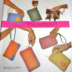 May include: An assortment of wristlets in various colors and designs. The wristlets include a blue one with a yellow flower, a pink one with a bow, and a green one with floral embroidery. The text "introducing... the wristlet" is visible.