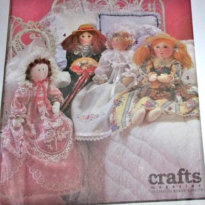 May include: A collection of handmade cloth dolls, each with unique outfits and hairstyles. The dolls are dressed in vintage-style dresses with lace and floral patterns. One doll holds a fan. The image is from a crafts magazine.