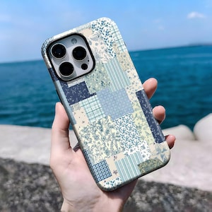 Könnte beinhalten: Eine Handyhülle mit Patchwork-Design in Blau-, Creme- und Grüntönen. Die Hülle hat eine glänzende Oberfläche und einen Kameraausschnitt. Das Design umfasst florale und geometrische Muster.