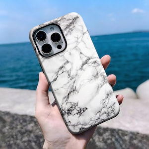 May include: A smartphone case with a white and grey marble effect. The case features a black camera surround and a glossy finish. The design mimics natural stone, providing a stylish and protective accessory.