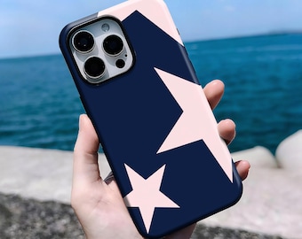 May include: A navy blue and pink phone case featuring two white stars. The case has a black border around the camera and a light pink top. The background is a blurred view of the ocean and sky.