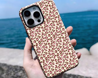 Peut inclure: Une coque de téléphone avec un motif léopard. La coque présente un fond beige avec des taches marron et roses. Les lentilles de la caméra sont visibles en haut à gauche. La coque est tenue devant un arrière-plan d'eau et de ciel bleus.