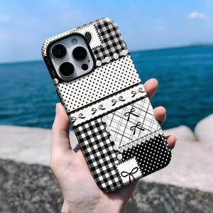 Pode incluir: Uma capa de telefone com padrão em preto e branco com um design de patchwork. A capa inclui bolinhas, xadrez vichy e laços. A capa é exibida em um fundo azul do oceano.