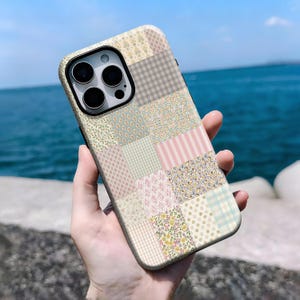 May include: A patchwork-style phone case featuring a variety of patterns and colors, including floral, striped, and checkered designs. The case has a neutral background with pastel pink, blue, and green accents. The phone case is designed to fit a smartphone.
