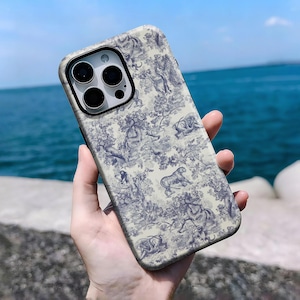Puede incluir: Funda de teléfono con fondo crema y estampado toile de Jouy azul con animales y follaje. La funda tiene un marco negro para la lente de la cámara. El fondo es el mar y el cielo.