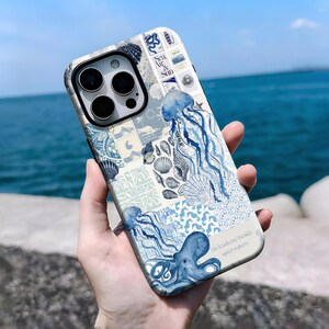 Puede incluir: Una funda de teléfono con un diseño marino, con medusas azules, un pulpo y conchas marinas. La funda tiene un collage de patrones y el texto "Sea, Air & Sun" y "He leads me beside quiet waters".