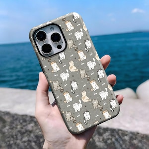 May include: A gray phone case featuring a repeating pattern of cartoon cats in various poses. The cats are in shades of gray, white, and tan, with small fish icons scattered throughout the design. The case has a black camera module.