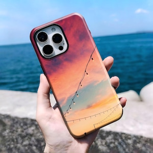 May include: A smartphone case featuring a sunset sky gradient transitioning from deep red to orange and yellow. The design includes thin black lines representing strings of small glowing fairy lights draped diagonally across the back surface.