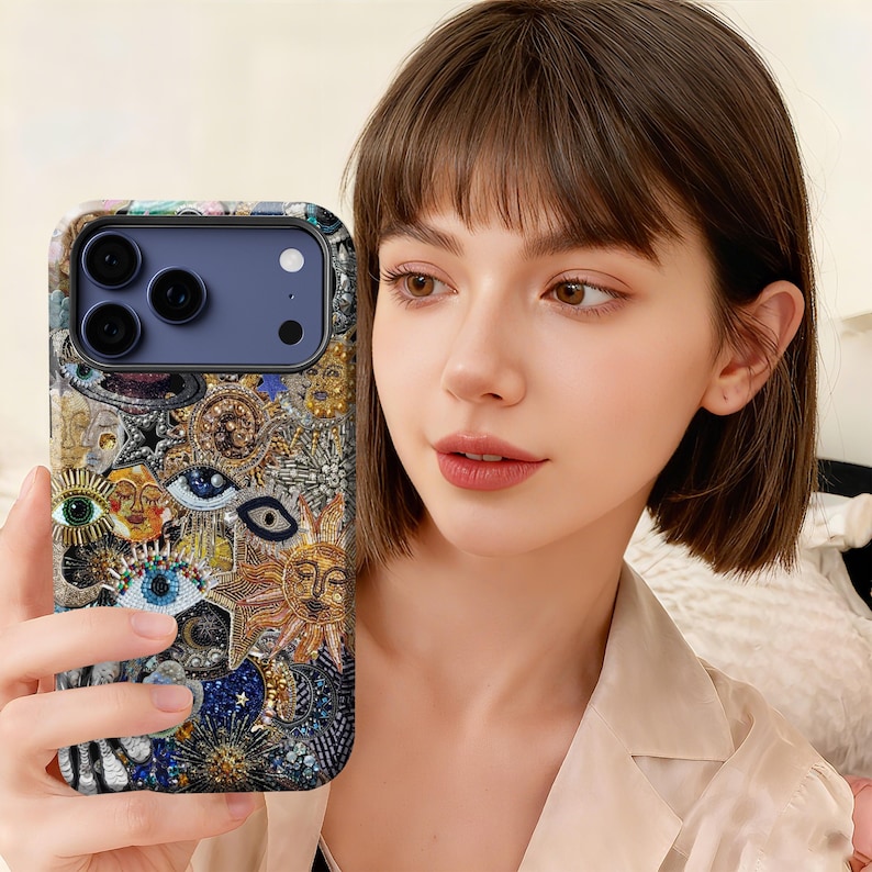 May include: A detailed phone case with an intricate design, featuring celestial and eye symbols in gold, blue, and silver. The case has a textured, artistic look. The phone case is designed for a modern smartphone, offering both style and protection.
