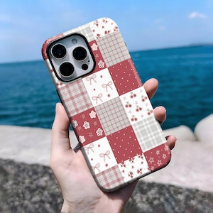 May include: A patchwork-style phone case featuring a mix of red, white, and gray squares. The design includes patterns of bows, cherries, flowers, and plaid. The case has a red border and a camera cutout.