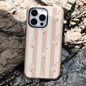 May include: A phone case featuring a repeating pattern of ducks with blue bows, set against a backdrop of alternating pink and cream vertical stripes. The case has a glossy finish and a camera cutout.