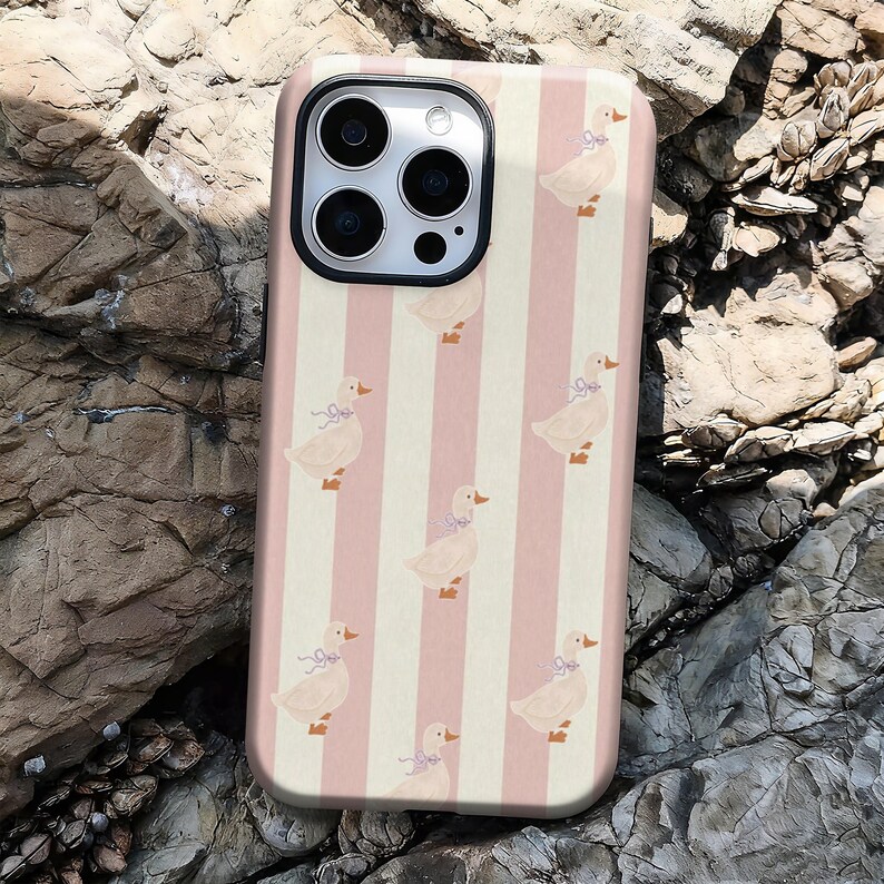 May include: A phone case featuring a repeating pattern of ducks with blue bows, set against a backdrop of alternating pink and cream vertical stripes. The case has a glossy finish and a camera cutout.