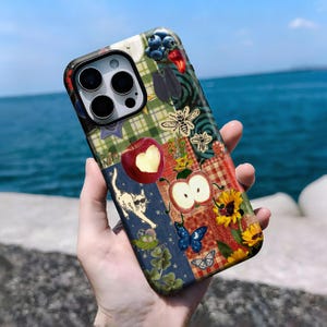 May include: A patterned phone case with a patchwork design. The case features apples, bees, sunflowers, and butterflies. The design includes plaid and floral elements, with a cat wearing sunglasses. The case is held against a backdrop of the sea.