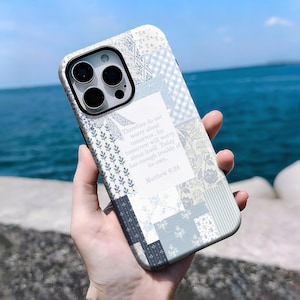 Può includere: Una custodia per telefono a fantasia patchwork nei toni del blu, bianco e grigio. La custodia presenta una citazione da Matteo 6:34. La custodia del telefono è tenuta contro uno sfondo dell'oceano.