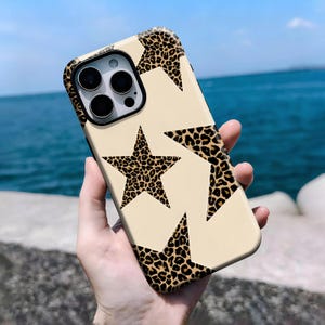 Op de afbeelding: Een telefoonhoesje met een beige achtergrond en een patroon van luipaardprint sterren. De hoes heeft een zwarte rand en een camera-uitsparing. De sterren zijn gevuld met een bruine en zwarte luipaardprint.