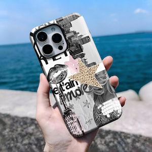 Pode incluir: Uma capa de telefone branca com um design de colagem com uma paisagem urbana em preto e branco, uma estrela rosa, uma estrela com estampa de leopardo, uma impressão de beijo e as palavras "e't'ain amore". A capa também tem um recorte preto para a lente da câmera.