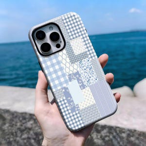 Puede incluir: Funda de teléfono de estilo patchwork en tonos azules y blancos. La funda presenta una variedad de patrones, incluyendo cuadros, florales y rayas. El fondo es el mar y el cielo.