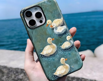 May include: A phone case featuring a watercolor painting of several yellow ducks swimming on a teal-colored pond. The ducks have orange beaks and are surrounded by water ripples. The case has a dark border around the camera.