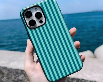 May include: Teal and turquoise striped phone case. The case has a black camera lens border and is held in a person's hand. The background shows the ocean and sky.