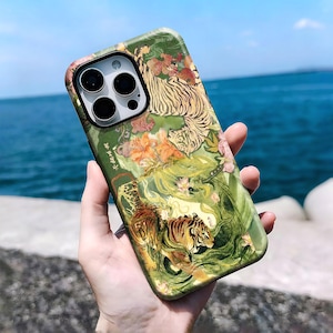 Pode incluir: Uma capa de smartphone com uma ilustração detalhada de dois tigres entre folhagem verde e detalhes florais laranja. O design inclui elementos de texto caligráfico subtis integrados na obra, com um recorte para a câmara fotográfica.