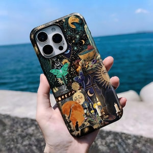 May include: A phone case featuring a celestial design with a night sky, moon, stars, and sun. The case has a dark background with a green butterfly, candles, and a sleeping face. The case is held in a hand.