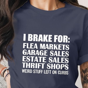 May include: Navy blue t-shirt with white text that reads "I Brake For: Flea Markets, Garage Sales, Estate Sales, Thrift Shops, Weird Stuff Left on Curbs." The shirt is a classic crew neck.