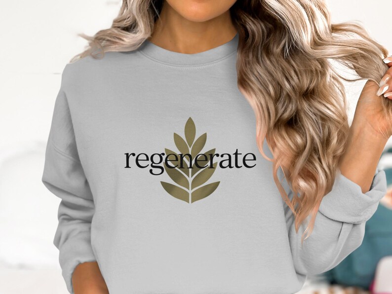 Puede incluir: Sudadera gris claro con la palabra "regenerate" en escritura negra y un dise&ntilde;o de hojas doradas. La sudadera es de cuello redondo y tiene mangas largas. El tema general es el bienestar y la naturaleza.