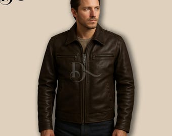 Puede incluir: Chaqueta de cuero marrón oscuro con cuello y cierre de cremallera. La chaqueta tiene dos bolsillos en el pecho con cremallera y un corte entallado. El modelo lleva una camisa marrón claro y vaqueros azules.
