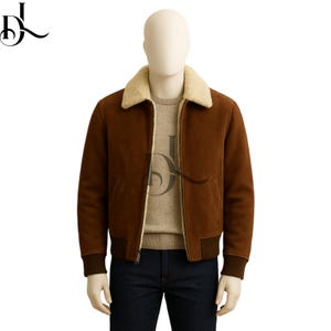 May include: A brown suede bomber jacket with a cream-colored shearling collar and a ribbed hem and cuffs. The jacket has a zip-up front and two front pockets. The model is wearing a light brown sweater and dark blue jeans.