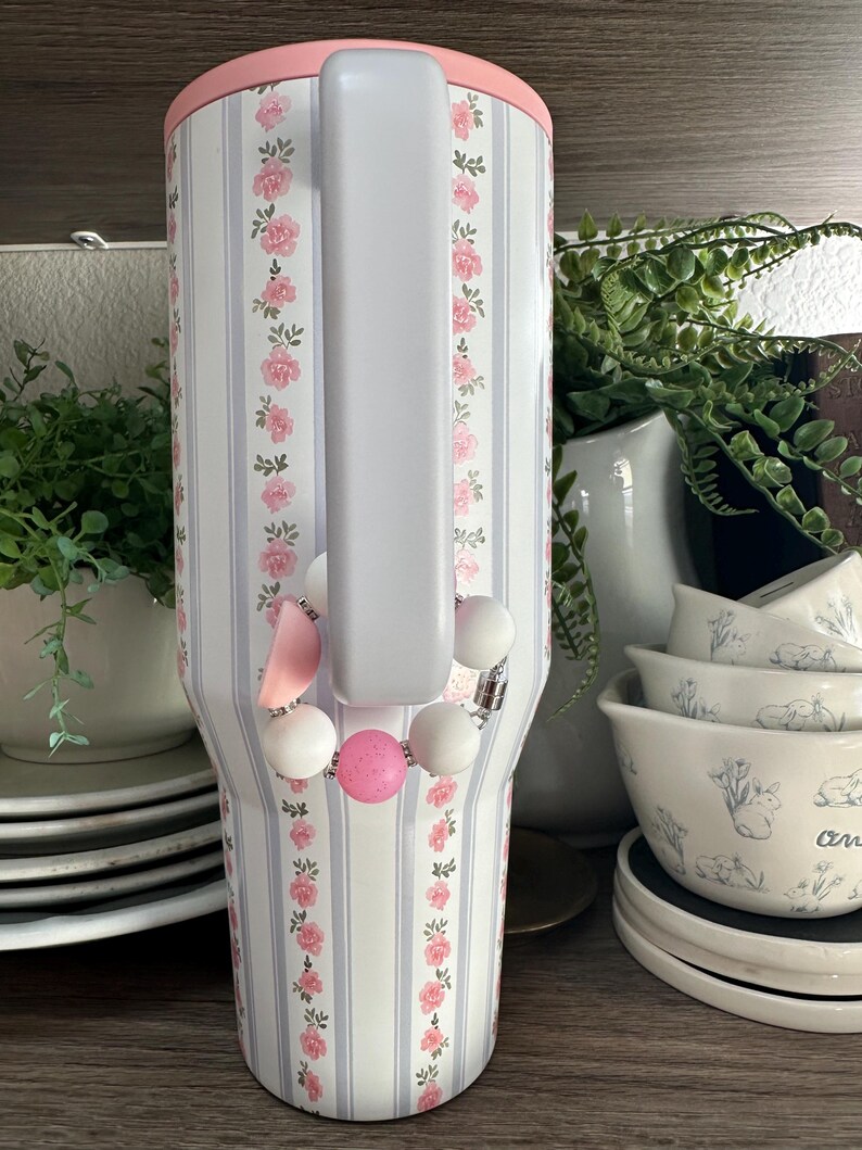 K&ouml;nnte beinhalten: Handgefertigtes Holzschild mit dem Wort "Welcome" in verspielter Schrift. Das Schild ist wei&szlig; lackiert mit einem Used-Look und mit einem floralen Design in Rosa- und Gr&uuml;nt&ouml;nen verziert. Es misst ca. 30 cm breit und 15 cm hoch.