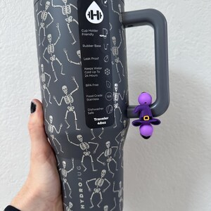 Puede incluir: Un vaso Hydrojug Traveler gris oscuro de 1,18 litros con un patr&oacute;n repetido de esqueletos blancos. Cuenta con un asa gris y un dije de sombrero de bruja morado. Sin BPA y apto para lavavajillas.