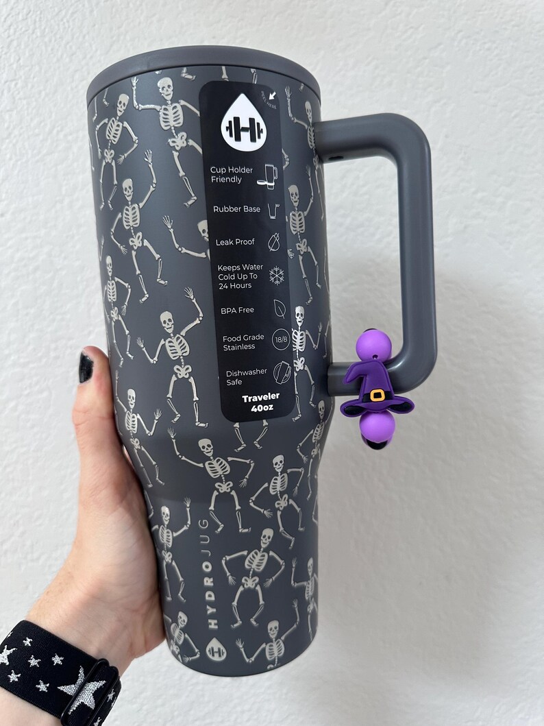 Puede incluir: Un vaso Hydrojug Traveler gris oscuro de 1,18 litros con un patr&oacute;n repetido de esqueletos blancos. Cuenta con un asa gris y un dije de sombrero de bruja morado. Sin BPA y apto para lavavajillas.