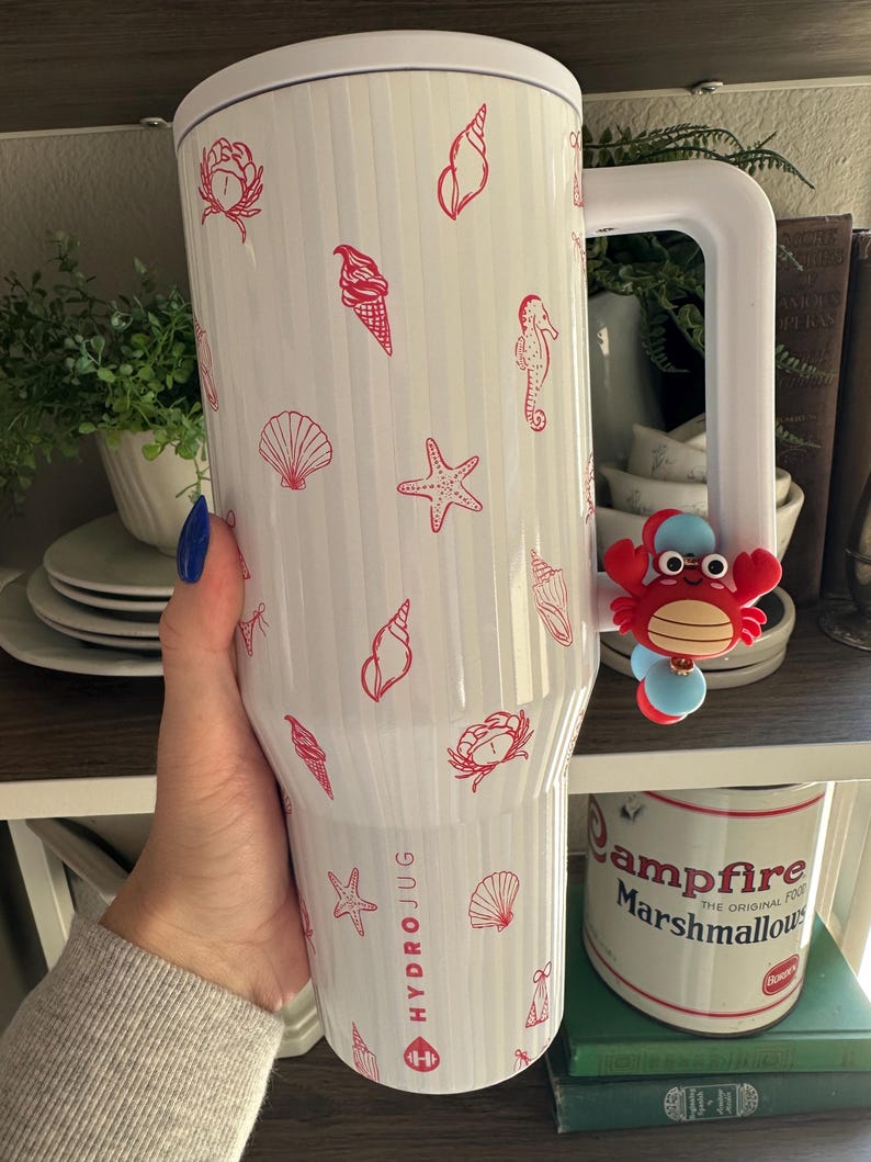 May include: White HydroJug with red seashell, starfish, and ice cream cone designs. The jug has a large white handle and a red crab charm. The text "HYDROJUG" is printed on the side.