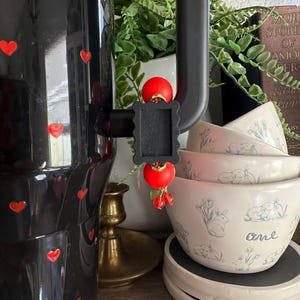 May include: A black coffee maker with red heart accents and a decorative red and black frame. Stacked white bowls with blue rabbit illustrations and the word "one" are also visible, along with a brass candlestick.