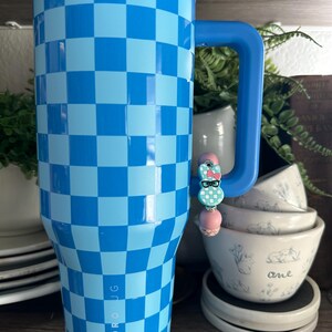 Op de afbeelding: Een blauw en lichtblauw geblokte Hydro Jug-beker met een blauw handvat. Een decoratieve bedel met een konijnenontwerp is aan het handvat bevestigd. De beker is ontworpen om dranken koud te houden.