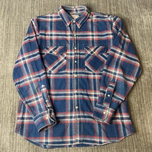 May include: A long-sleeved, button-down shirt in a classic plaid pattern. The shirt features a blue base with red and white intersecting lines, creating a checkered design. It has two chest pockets, a button-down collar, and buttoned cuffs. The shirt is made of a soft, woven fabric.