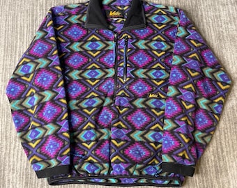 May include: A colorful fleece jacket with a geometric pattern in shades of purple, teal, yellow, and black. The jacket has a black collar, cuffs, and a zipper closure. The REI logo is visible on the collar and chest.