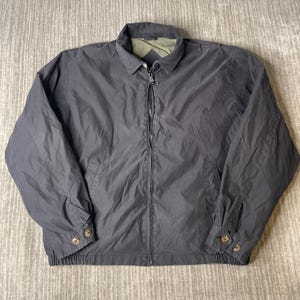 May include: A dark navy blue jacket with a collared neckline and a full-length zipper. The jacket has two buttoned cuffs and two front pockets. The interior lining is a light green color. The jacket is made of a lightweight material.