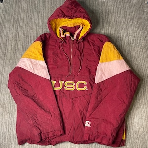 May include: Maroon hooded anorak jacket with gold and pink accents. The jacket features a half-zip closure, a hood with a gold lining, and the letters "USC" in gold across the chest. The Starter logo is visible on the lower right.