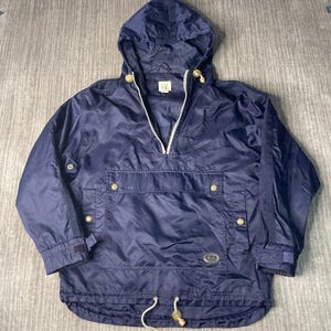May include: A navy blue anorak-style jacket with a hood and a half-zip closure. The jacket features a front pocket with snap closures, adjustable cuffs, and a drawstring hem. The Gap logo is visible on the inside of the hood.