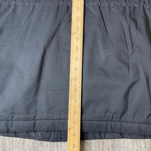 K&ouml;nnte beinhalten: Ein dunkelgraues Kleidungsst&uuml;ck mit einem Holzlineal, das vertikal in der Mitte platziert ist. Das Lineal zeigt Messungen von 50,8 cm bis 83,8 cm. Das Kleidungsst&uuml;ck hat ein strukturiertes Aussehen und sichtbare N&auml;hte.