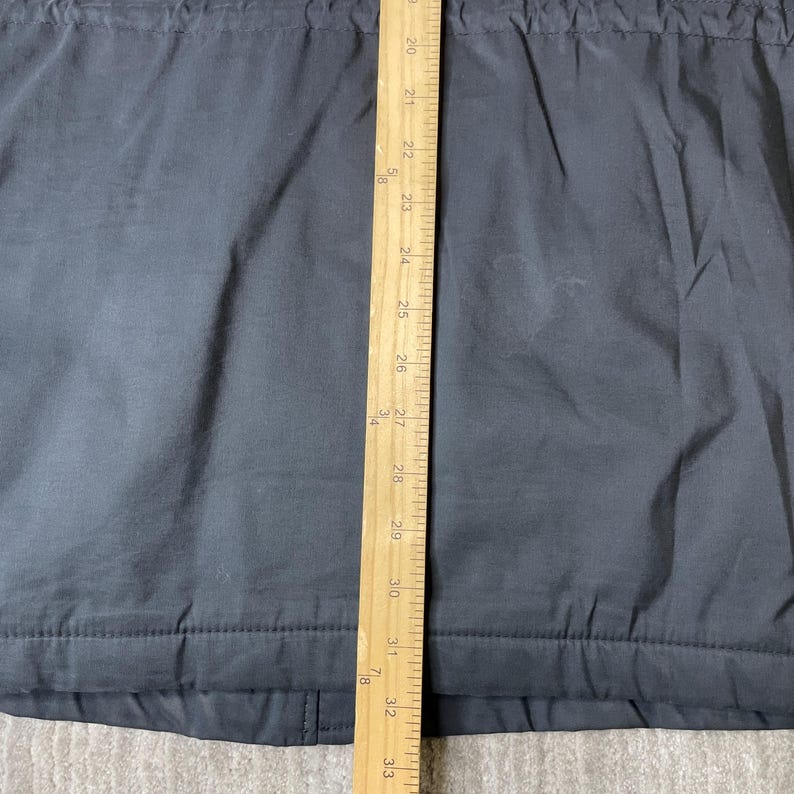 K&ouml;nnte beinhalten: Ein dunkelgraues Kleidungsst&uuml;ck mit einem Holzlineal, das vertikal in der Mitte platziert ist. Das Lineal zeigt Messungen von 50,8 cm bis 83,8 cm. Das Kleidungsst&uuml;ck hat ein strukturiertes Aussehen und sichtbare N&auml;hte.
